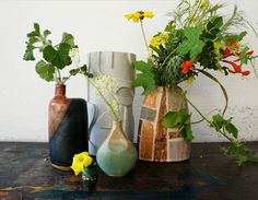 three vases with plants and flowers in them on a table next to a wall