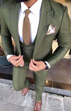 a man with a beard wearing a green suit and brown sandals is posing for the camera