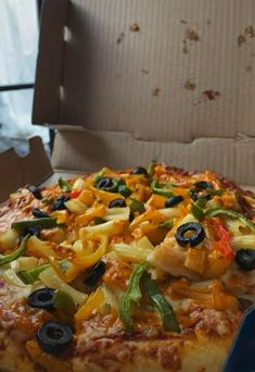 a pizza in a box with olives, peppers and cheese on the top is ready to be eaten