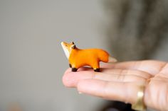 a tiny toy fox sitting on top of someone's hand