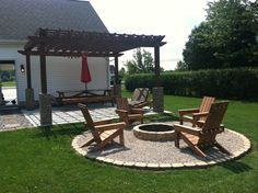 a fire pit surrounded by wooden chairs and an umbrella in the middle of a yard