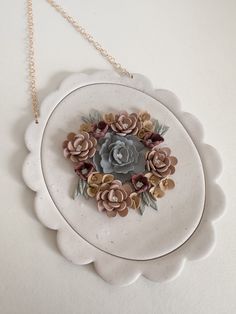 a white plate with flowers on it and a gold chain hanging from the side,