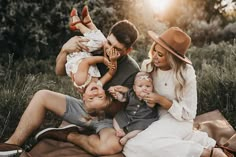 a man and woman holding two babys in their arms while they sit on the ground