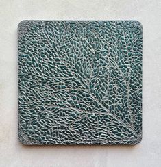 a close up of a square metal object on a white wall with blue paint and green leaves