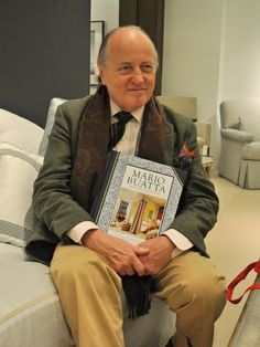 an older man sitting on a bed holding a book