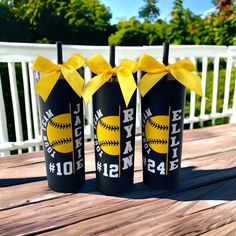 three black tumblers with yellow ribbons and baseballs on them sitting on a wooden table