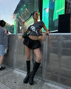 a woman standing next to a metal fence on top of a stage wearing black boots