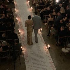 a man and woman walking down a long aisle with lit candles on the floor in front of them