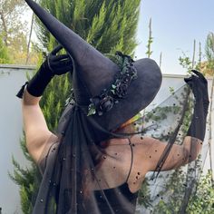 a woman wearing a witches hat and black dress with her hands in the air while standing outside