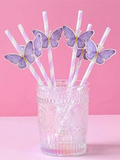 purple and white striped paper straws in a clear glass vase on a pink background