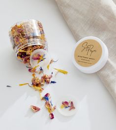 a small jar filled with dried flowers next to a white cup on top of a table