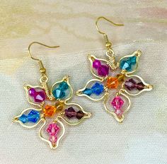 two pairs of earrings with multicolored stones in gold tone setting on white fabric