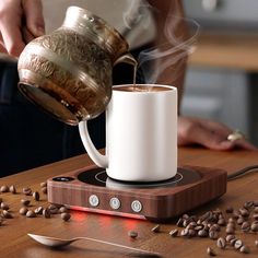 a person pours coffee into a white mug on top of a wooden table surrounded by coffee beans