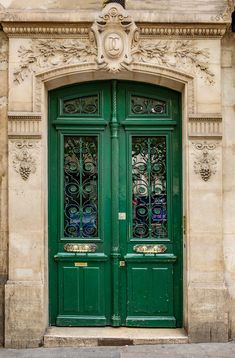 an ornately decorated green door in front of a stone building with glass panels on the doors