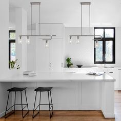 a white kitchen with two stools next to the counter top and an open window