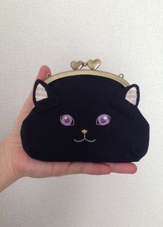 a hand holding a black cat purse with purple eyes