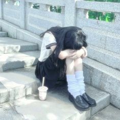 a woman sitting on the steps with her head in her hands and holding a cup