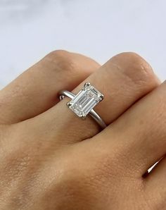 a woman's hand with a diamond ring on top of her finger and an emerald stone in the middle