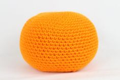 an orange crocheted ball sitting on top of a white surface with no background