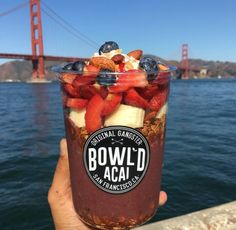 a person holding up a cup with fruit and yogurt in front of the golden gate bridge