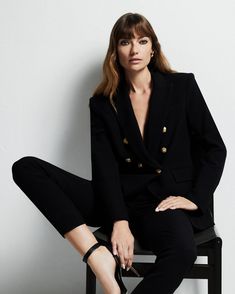 a woman sitting on top of a chair wearing black pants and a blazer jacket