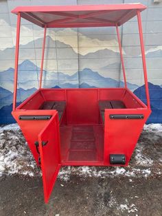 a red cart sitting in the snow next to a wall with mountains painted on it