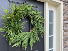 a wreath hanging on the front door of a house with green leaves and branches around it