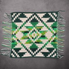 a green and white rug with fringes on the floor next to a gray wall