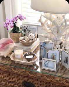 a wicker table topped with pictures and candles next to a basket filled with seashells