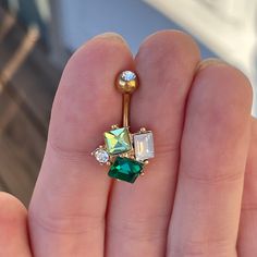 a person holding a green and white jeweled navel ring