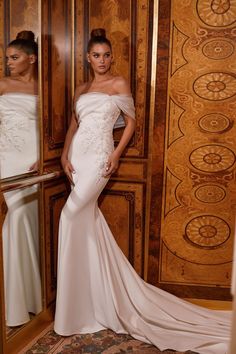 two women standing in front of wooden doors wearing white gowns and one is looking at the camera