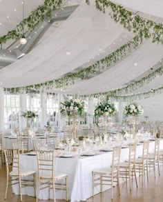 the tables are set with white linens and greenery hanging from the ceiling above them