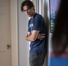 a young man leaning against a wall with his arms crossed