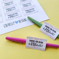 two name tags are sitting on top of a pen next to some pens and paper