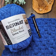 a blue crochet blanket next to a ball of yarn with a pen on it