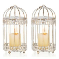 two white candles are in a birdcage with filigrees on the sides