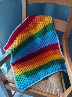 a multicolored crocheted blanket sitting on top of a wooden rocking chair