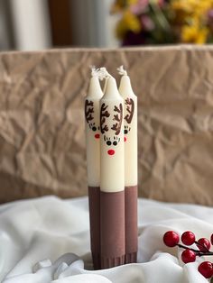 two candles with reindeer faces on them sitting on a white cloth next to some berries