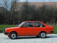 an orange car parked in front of a building on a brick sidewalk next to grass and trees