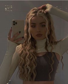 a woman with long curly hair is taking a selfie in front of a mirror