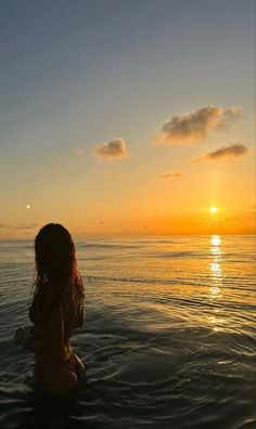 a woman is sitting in the water at sunset