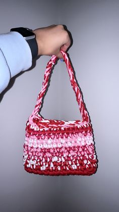 a hand holding a red and white bag with pink stripes on the bottom, in front of a gray background