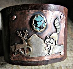 Into the Wild Distressed Wide Leather Cuff bracelet by Weathered Soul Jewelry, raccoon, artisan made, rustic, Buck, Deer, Antlers, OOAK, USA This is truly and amazing piece. It is wide Buffalo hide distressed leather with 2 heavy duty bronze snaps set for a 7 inch wrist size. Keep in mind they fit a little snugger than usual with wide leather so this could fit a tad smaller wrist still. Genuine turquoise matrix stone set in silver on copper. Raccoon and Deer are sterling as well as the mountains Handmade Adjustable Nature-inspired Cuff Bracelet, Rustic Cuff Bracelets As Gift, Rustic Cuff Jewelry For Gifts, Rustic Cuff Jewelry Gift, Rustic Cuff Jewelry As A Gift, Artisan Stamped Cuff Bracelet As Gift, Artisan Stamped Cuff Bracelet Gift, Bohemian Stamped Cuff Bracelet For Gift, Bohemian Stamped Cuff Bracelet Gift