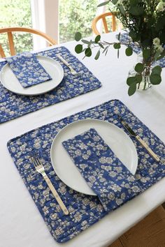 two place settings on a white table cloth with blue and white flowers in vases