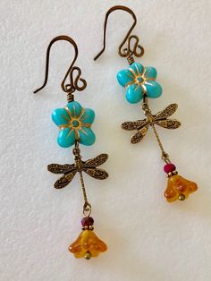 "Adorable turquoise blue Czech glass puffed daisies with topaz yellow bellflowers and vintage bronze stamped dragonfly charms. Matte turquoise 14 mm Czech glass puffy 5 petal flowers are etched with metallic gold and wire wrapped in vintage bronze with 6 x 9 mm translucent topaz yellow bellflowers accented with tiny burnt orange crystals. Lightweight dangles hang on handmade and hammered vintage bronze ear wires. Total drop length is 2 1/2\"." Vintage Turquoise Flower Earrings, Vintage Turquoise Dangle Flower Earrings, Turquoise Flower Charm Earrings For Gift, Turquoise Flower Earrings As A Gift, Gift Turquoise Flower Charm Earrings, Gift Turquoise Flower Earrings, Turquoise Nickel Free Flower Earrings, Nickel Free Turquoise Flower Earrings, Turquoise Dangle Earrings With Flower Charm