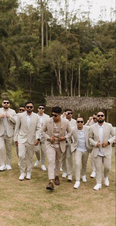 a group of men in suits and sunglasses walking across a grass covered field with trees in the background