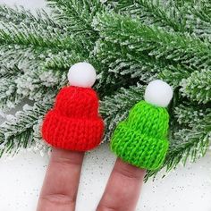 two small knitted hats sitting on top of a persons finger next to a pine tree