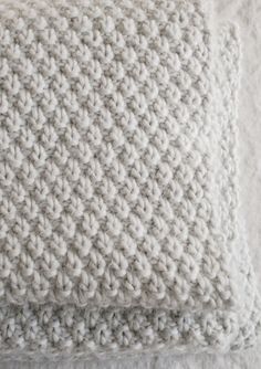 a white knitted pillow sitting on top of a bed