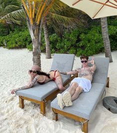 two people laying on lounge chairs at the beach