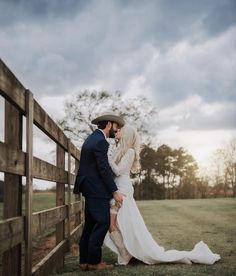 a bride and groom kissing in front of a wooden fence on their wedding day at sunset